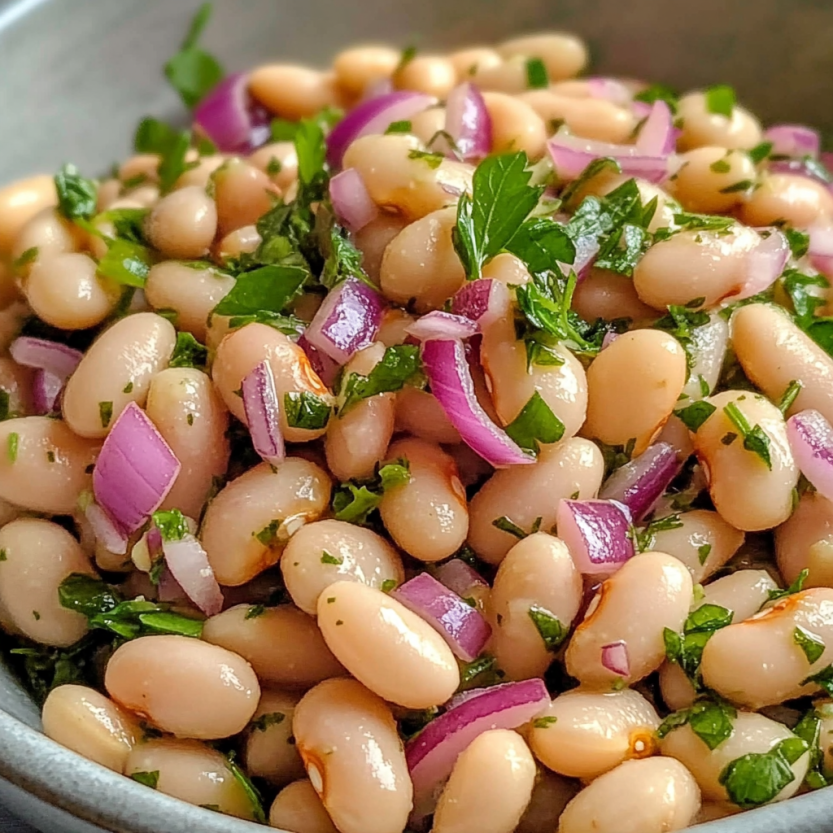 A bowl of white bean salad with onions and herbs.