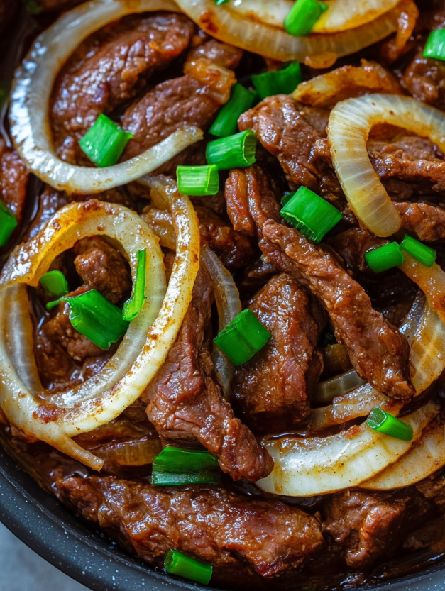 A dish of beef with onions and green onions.