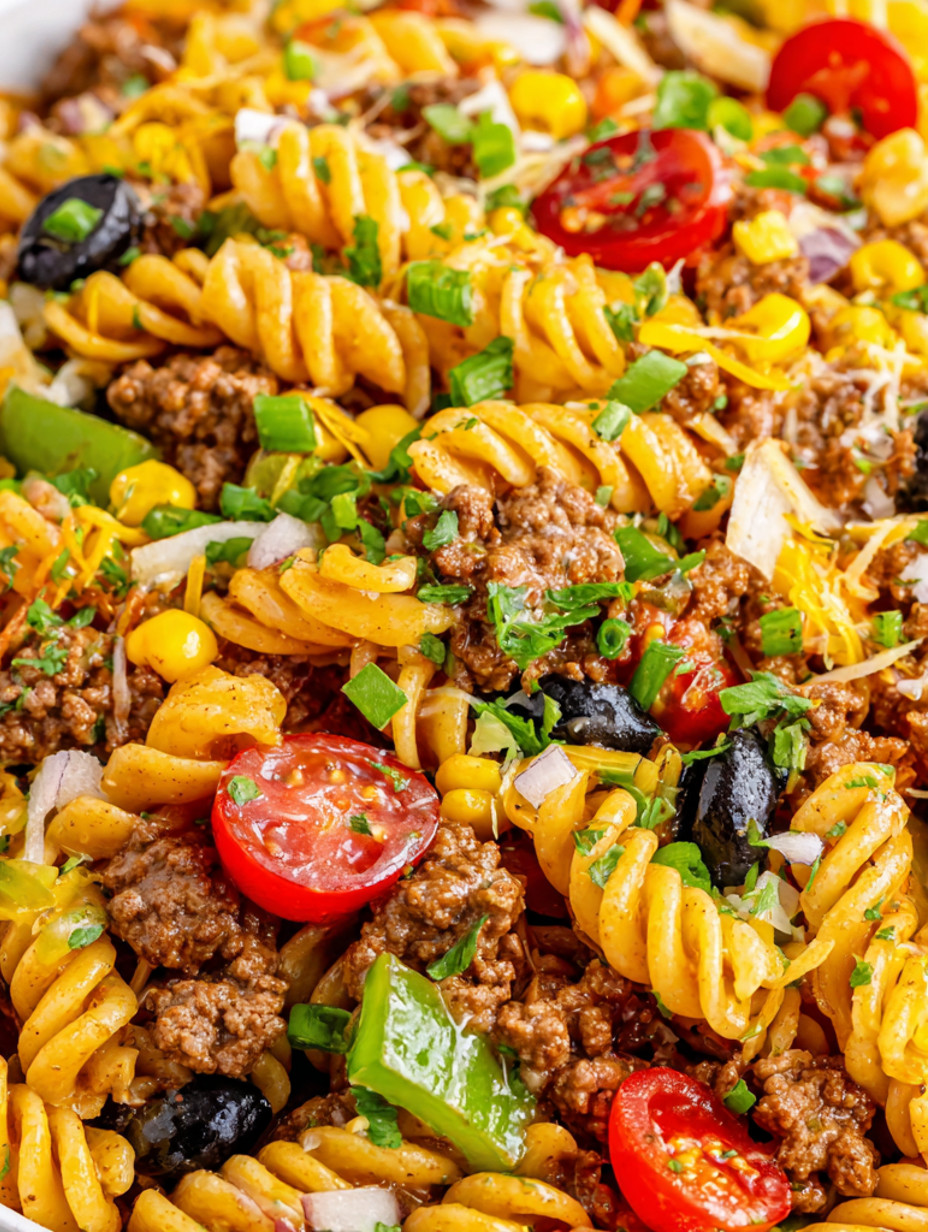 A dish of pasta salad with tomatoes, olives, and meat.