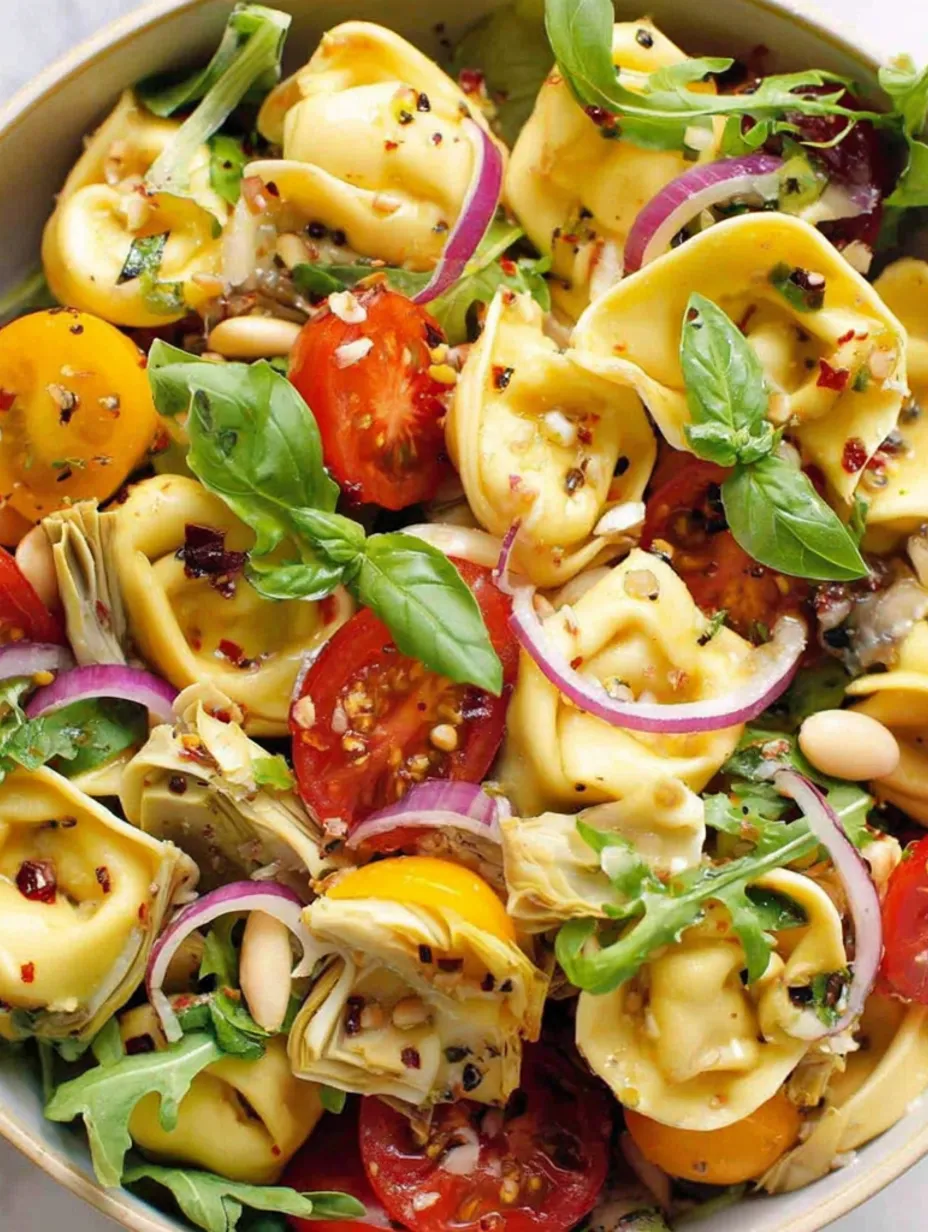 A bowl of pasta salad with tomatoes, spinach, and tortellini.