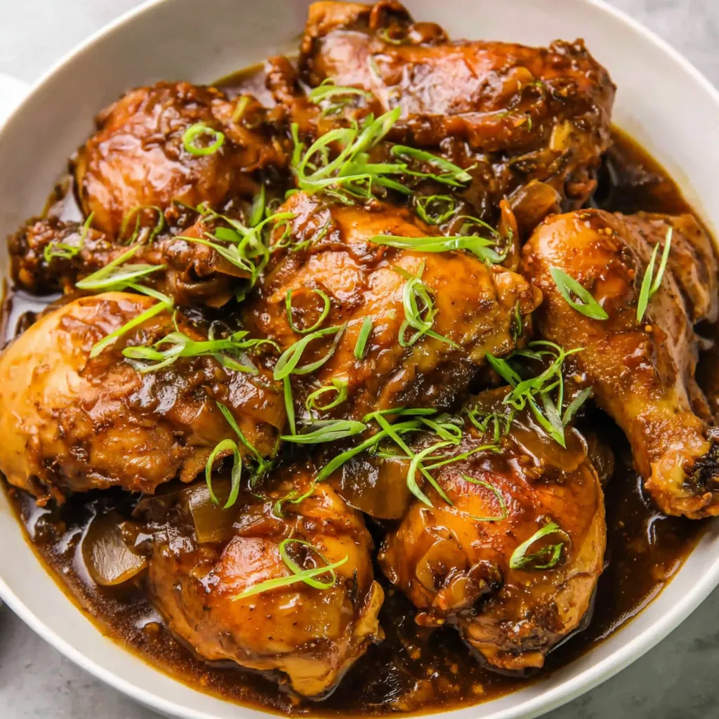 A bowl of chicken adobo with green onions.