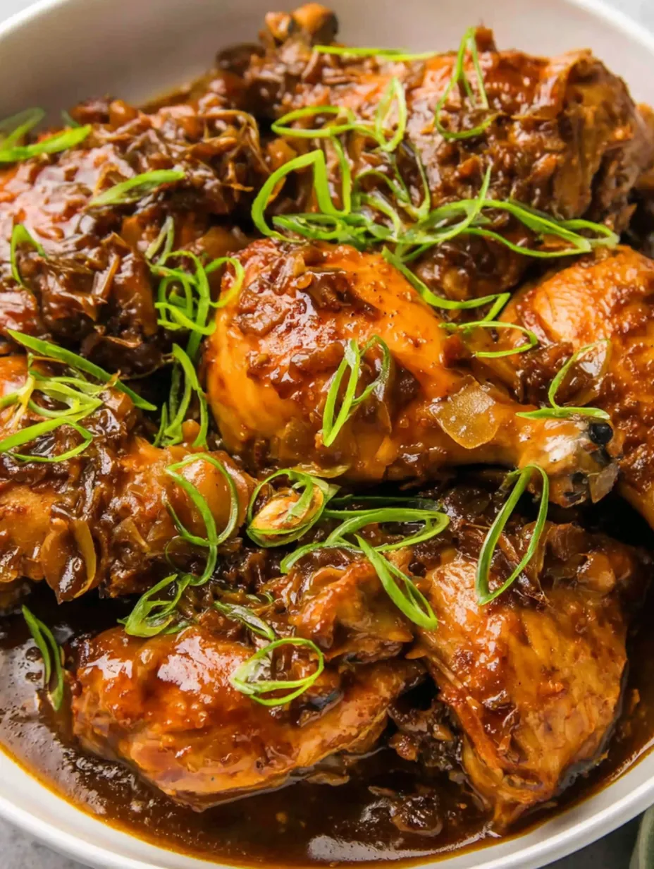 A close up of chicken with green onions and brown sauce.