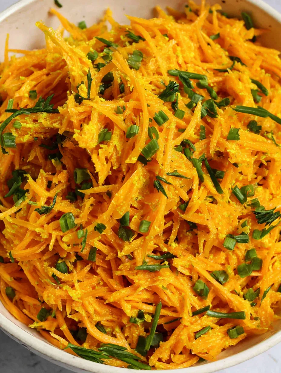 A bowl of grated carrots with green toppings.