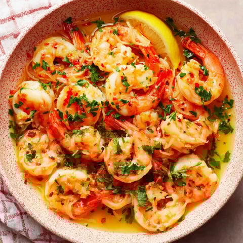 A bowl of shrimp scampi with a lemon wedge on top.