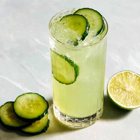 A glass of cucumber gin fizz cocktail with a slice of cucumber on the side.