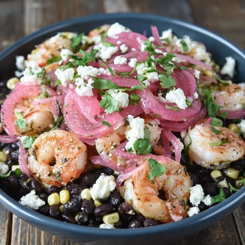 A bowl of black bean shrimp salad with corn and pickled onions.