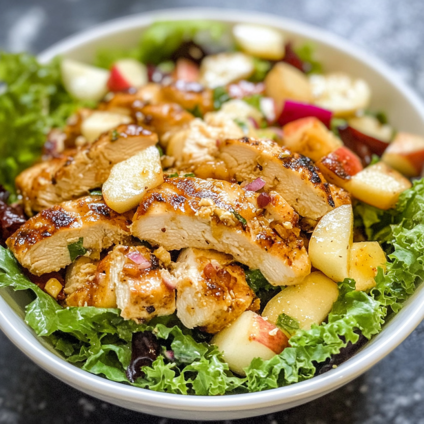 A bowl of salad with grilled chicken, white cheddar, and apples.