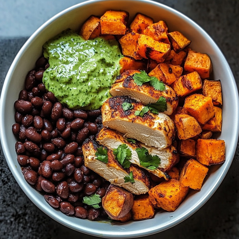 Un bol de nourriture avec des morceaux de poulet, des haricots noirs, de la patate douce, et du coriandre frais.