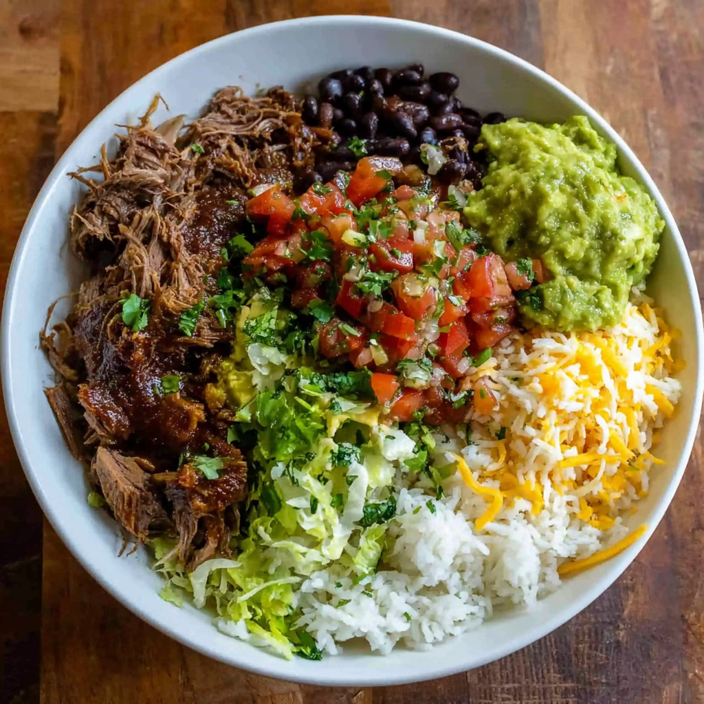A bowl of food with rice, beans, tomatoes, lettuce, and meat.