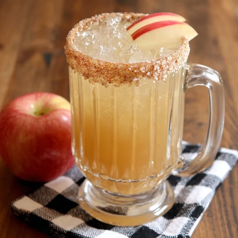 A glass of apple cider with a slice of apple on top.